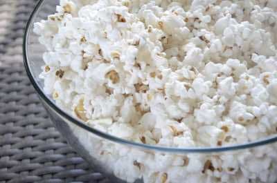 Glass bowl filled with freshly popped popcorn on a woven surface.