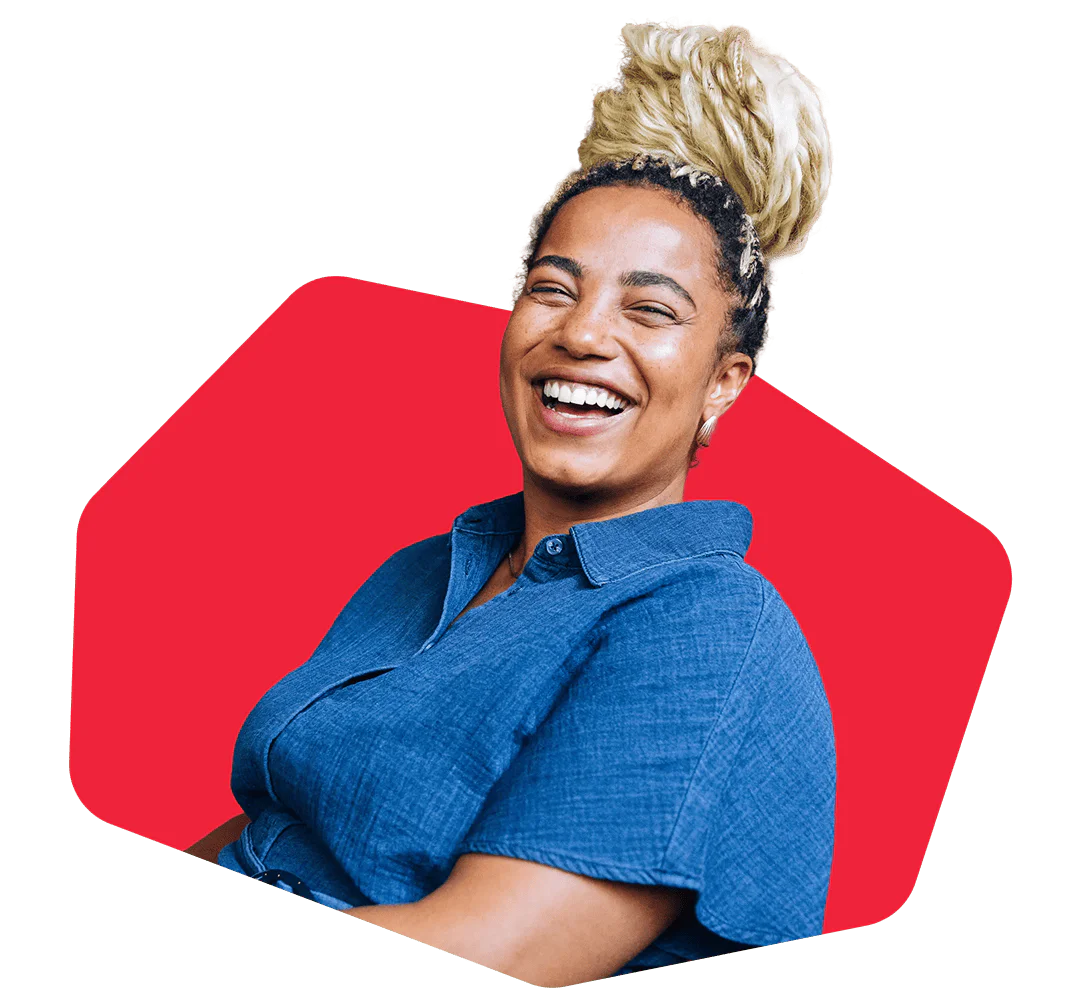 Happy woman with a high blonde hairstyle, wearing a blue shirt, smiling against a red background.