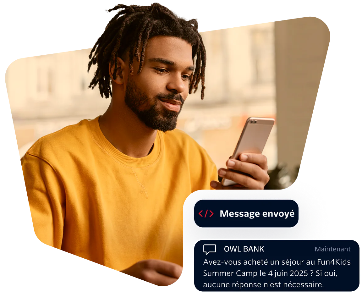 Young Man Receiving a Bank Message on Smartphone Man in yellow shirt looking at phone with a message from Owl Bank about a summer camp purchase.