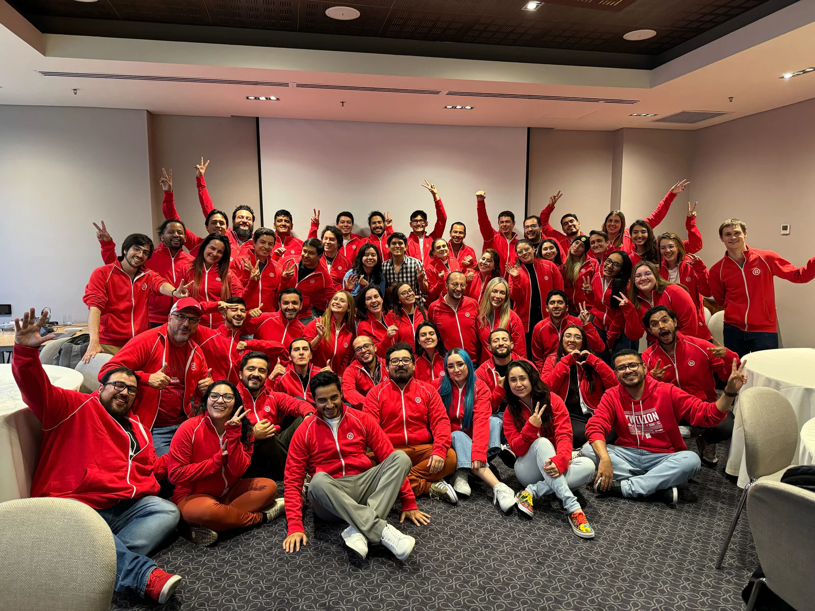A large group of people wearing matching red hoodies posing together in a conference room.