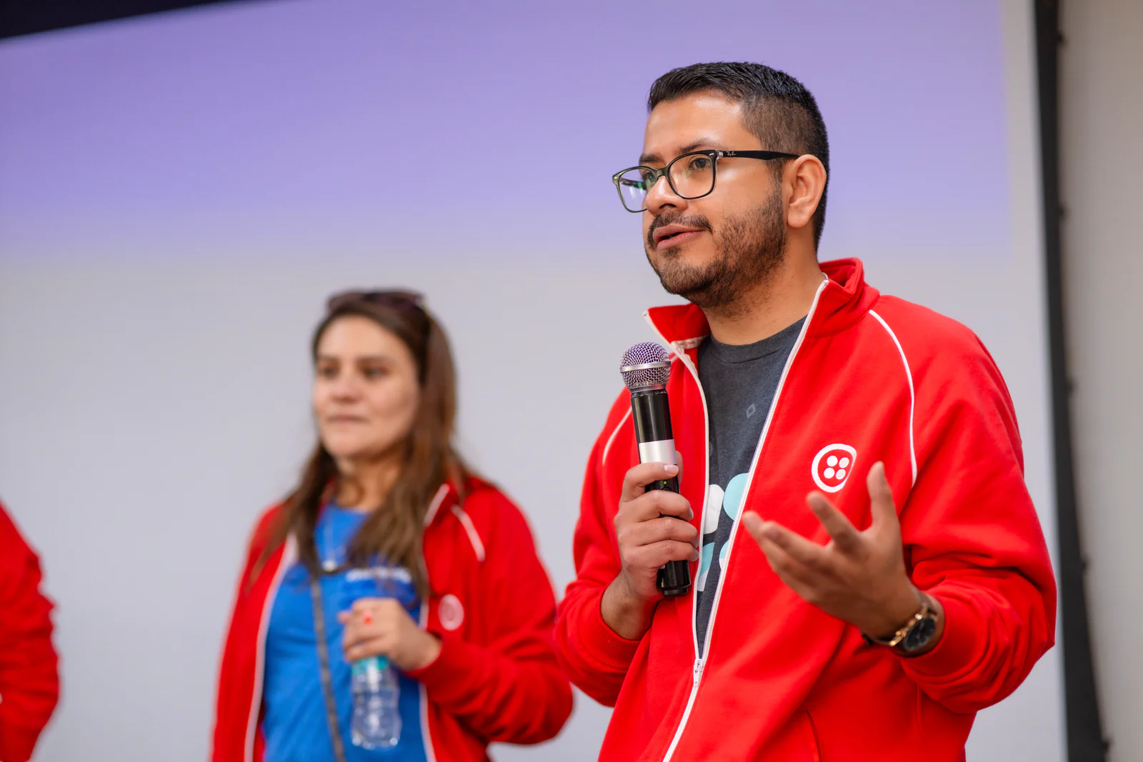 Two people in red jackets with microphones speaking at an event.