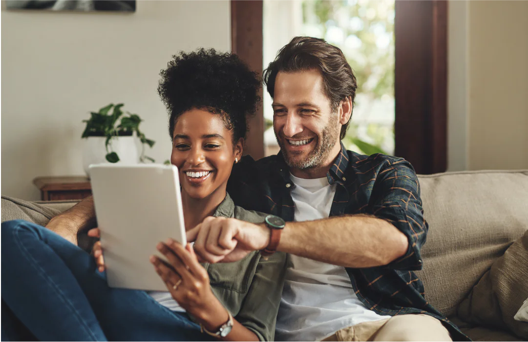 Smiling couple sitting on a couch, looking at a tablet together.