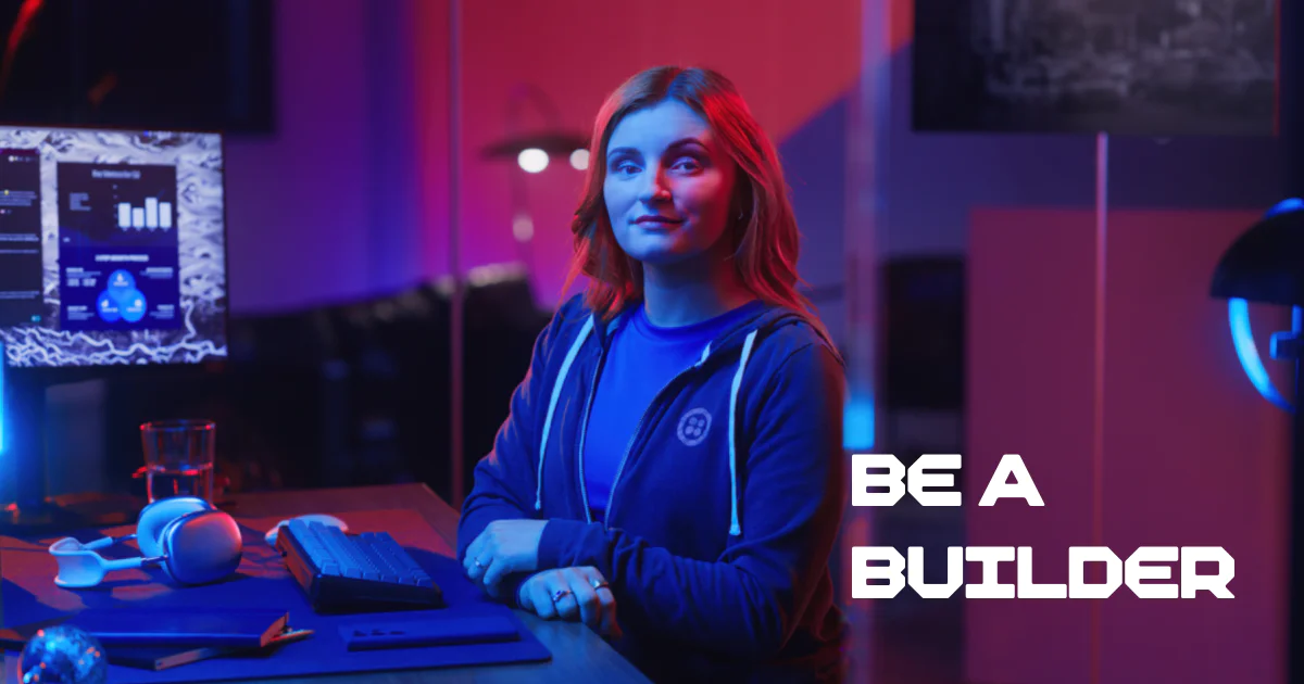 Woman in blue shirt and hoodie sitting in a tech office with computers and Be a Builder text on the right.