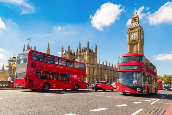 Red double-decker buses in front of Big Ben and the Houses of Parliament on a sunny day.