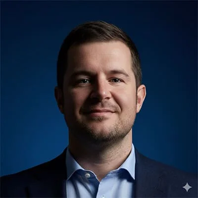 Headshot of a man in a suit and blue shirt with a dark blue background.