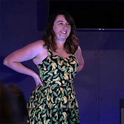 Smiling woman wearing a banana-patterned dress standing and speaking at an event