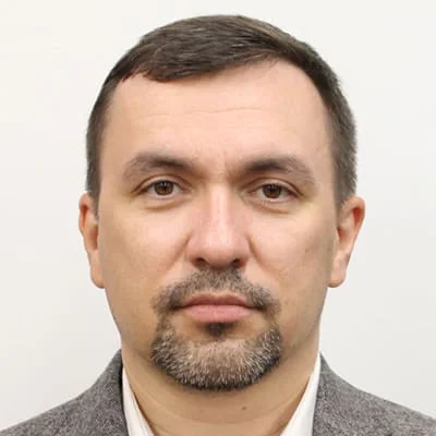 Headshot of a man with a short beard, wearing a gray jacket and white shirt, against a white background.