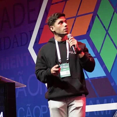 A man with white lanyard and badge speaks at a conference holding a microphone and remote.