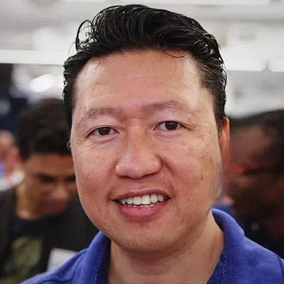 Close-up of a smiling man with short black hair at a social gathering.