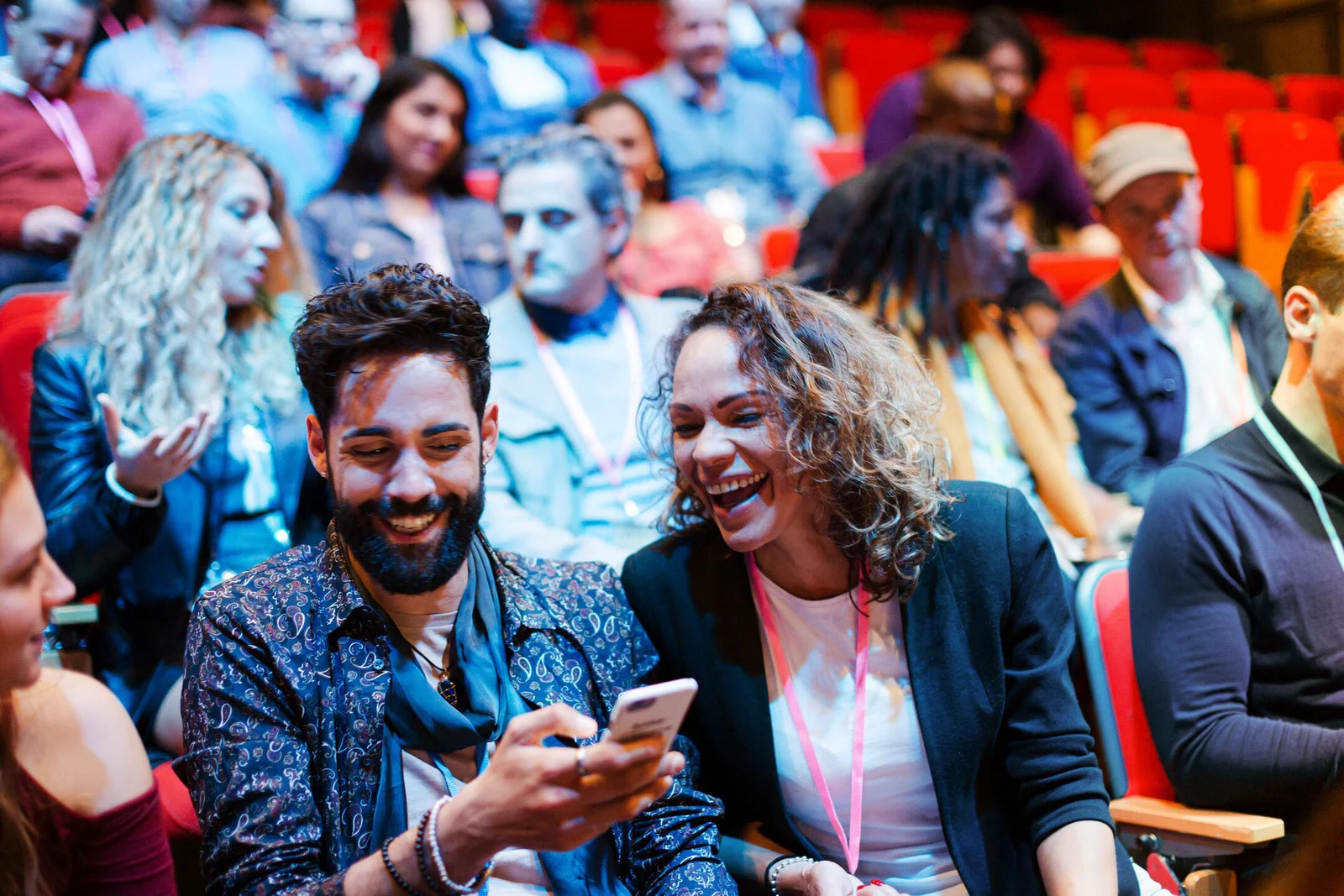 Group of people sitting in red chairs at an event, smiling and talking, with some using phones