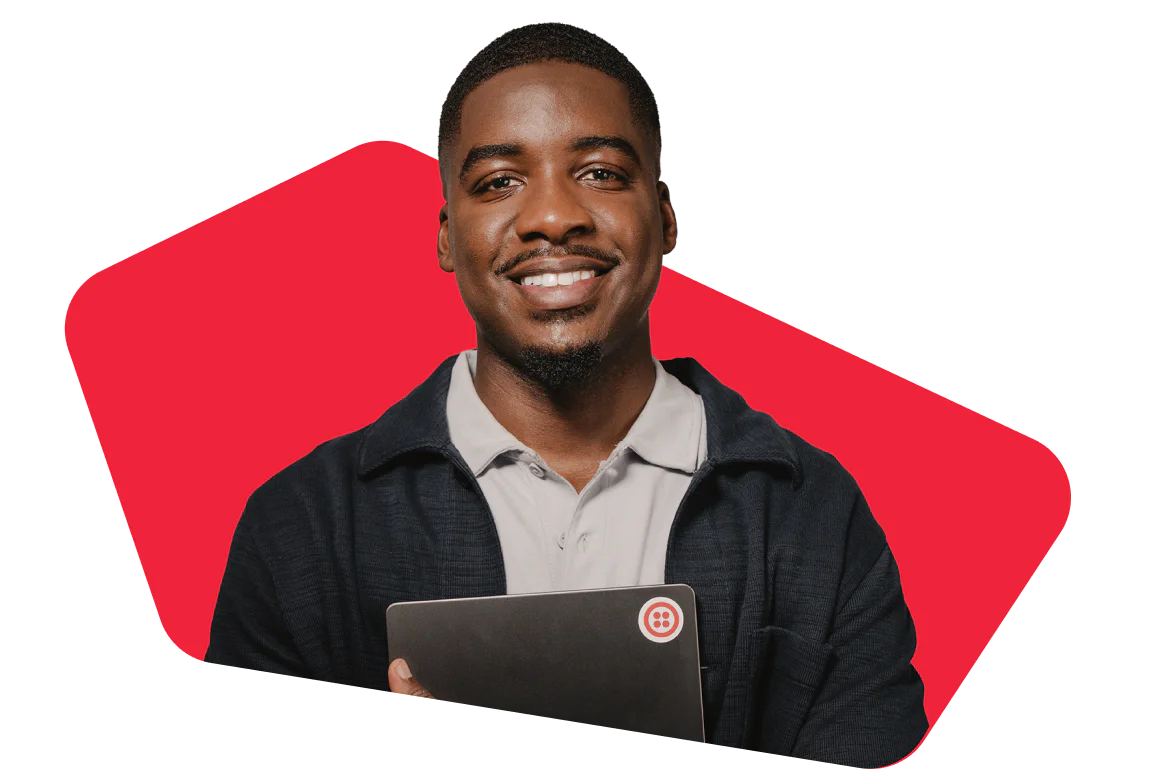 Smiling man holds a laptop in front of a red geometric background.