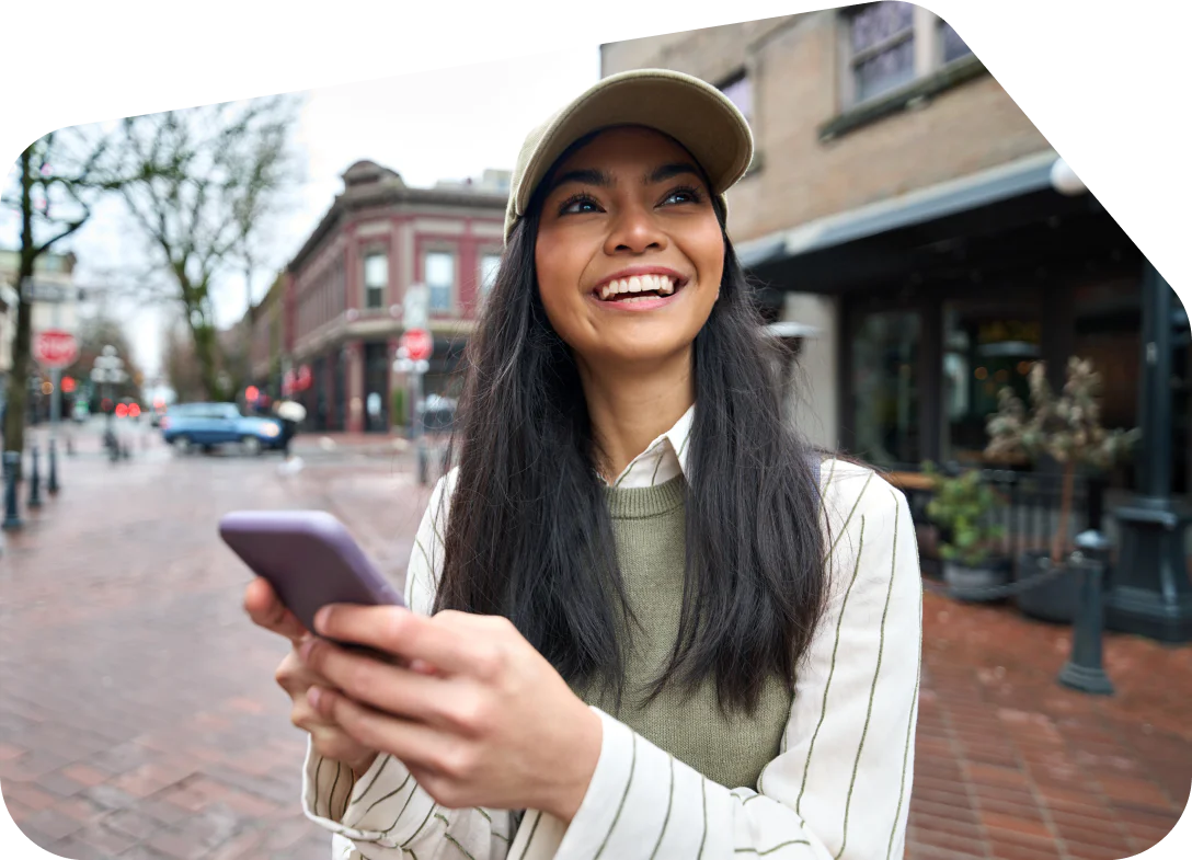 Smiling woman in cap using a smartphone on a brick-paved street