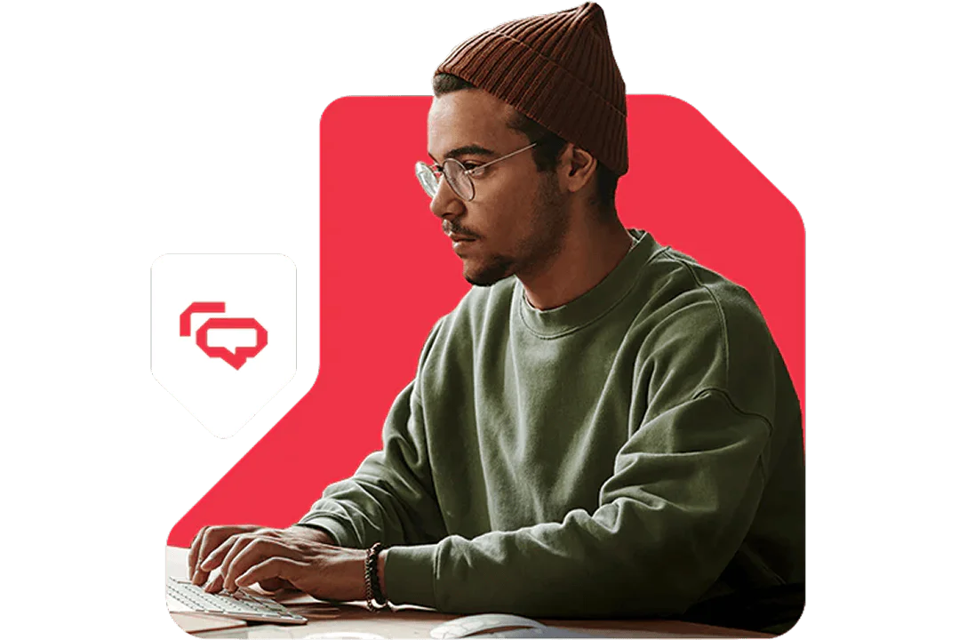 Man in green sweater and brown beanie typing on a keyboard with a red backdrop.