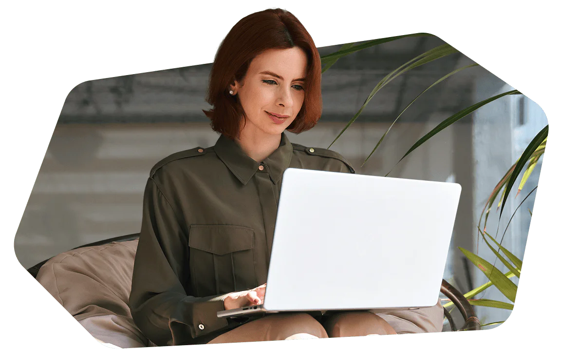 Woman in a green blouse using a white laptop while sitting indoors in a cozy chair.