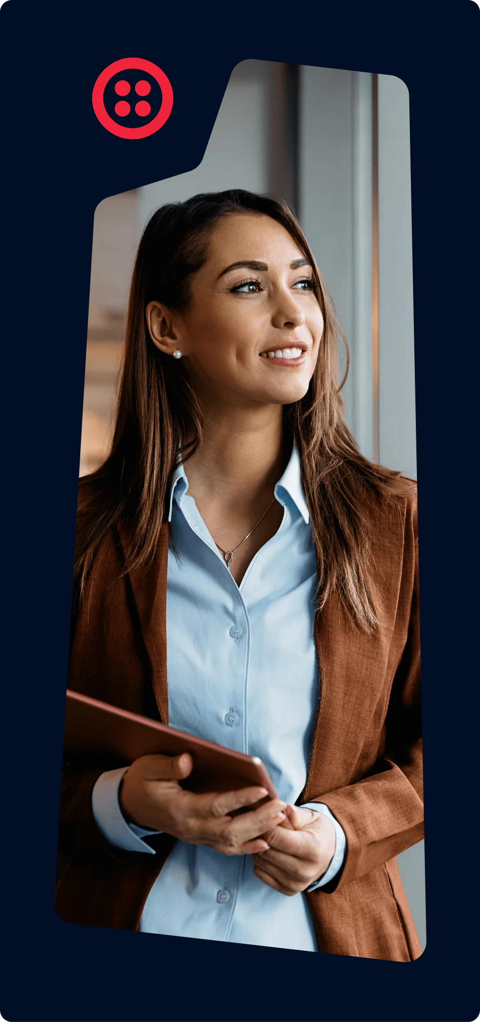 Woman in a brown blazer holding a tablet and smiling while looking to the side.