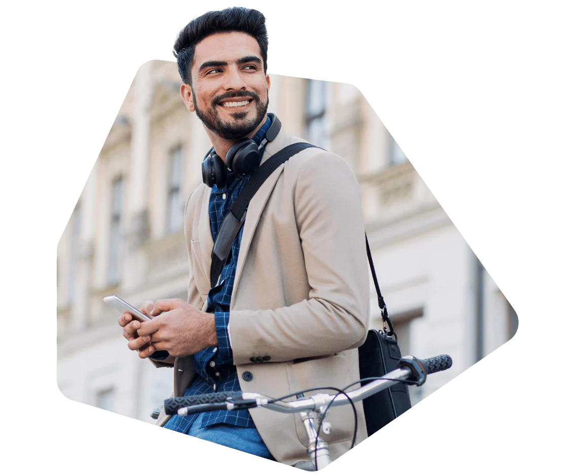 Smiling man wearing headphones and a beige blazer, holding a phone while resting on a bike.