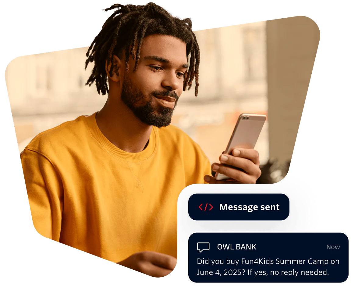 Young Man Receiving a Bank Message on Smartphone Man in yellow shirt looking at phone with a message from Owl Bank about a summer camp purchase.