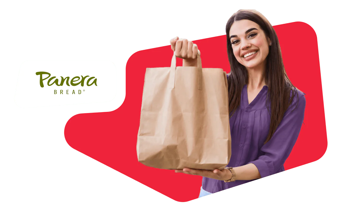 Smiling Woman Holding Panera Bread Bag Woman smiling and holding a brown paper bag with Panera Bread logo in the background.