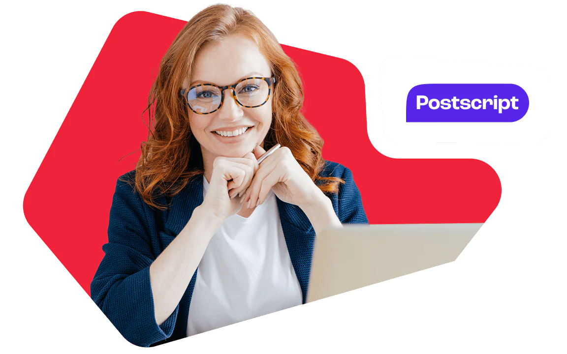 Smiling Redhead Woman with Glasses Working on Laptop Redheaded woman with glasses smiles, sitting at a laptop, with the Postscript logo in the background.
