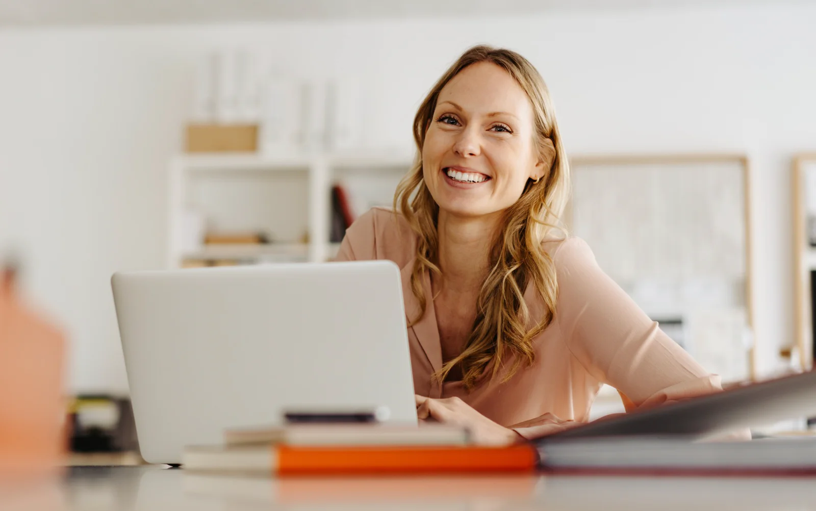 Woman smiling while using a laptop at a desk in a bright office.