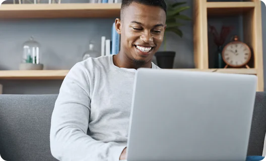 Respond in real time: The secret to staying relevant to consumers Man sitting on a couch and smiling at a laptop screen with bookshelves in the background.