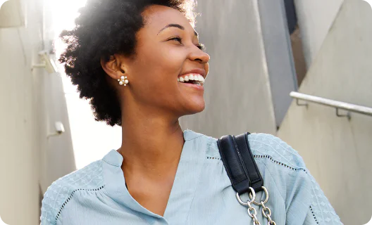 Choose the right channels to drive engagement Woman with curly hair and flower earrings smiling while standing outdoors wearing a blue top.