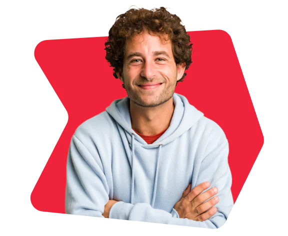 Man with curly hair and light blue hoodie smiling with arms crossed in front of a red background.