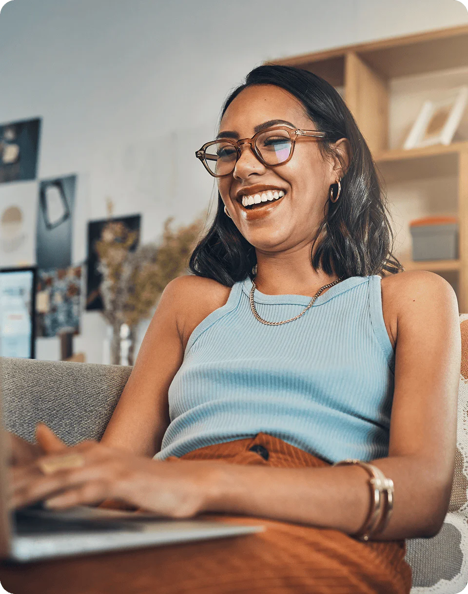 Smiling woman with glasses using a laptop while sitting on a couch.