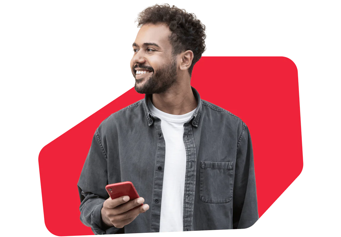 Smiling man holding a smartphone with a red background A smiling man in a gray shirt holds a smartphone against a red background