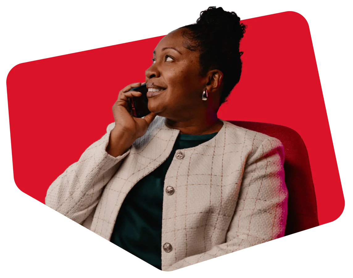 Woman smiling while speaking on her phone, wearing a light blazer, with a red background.