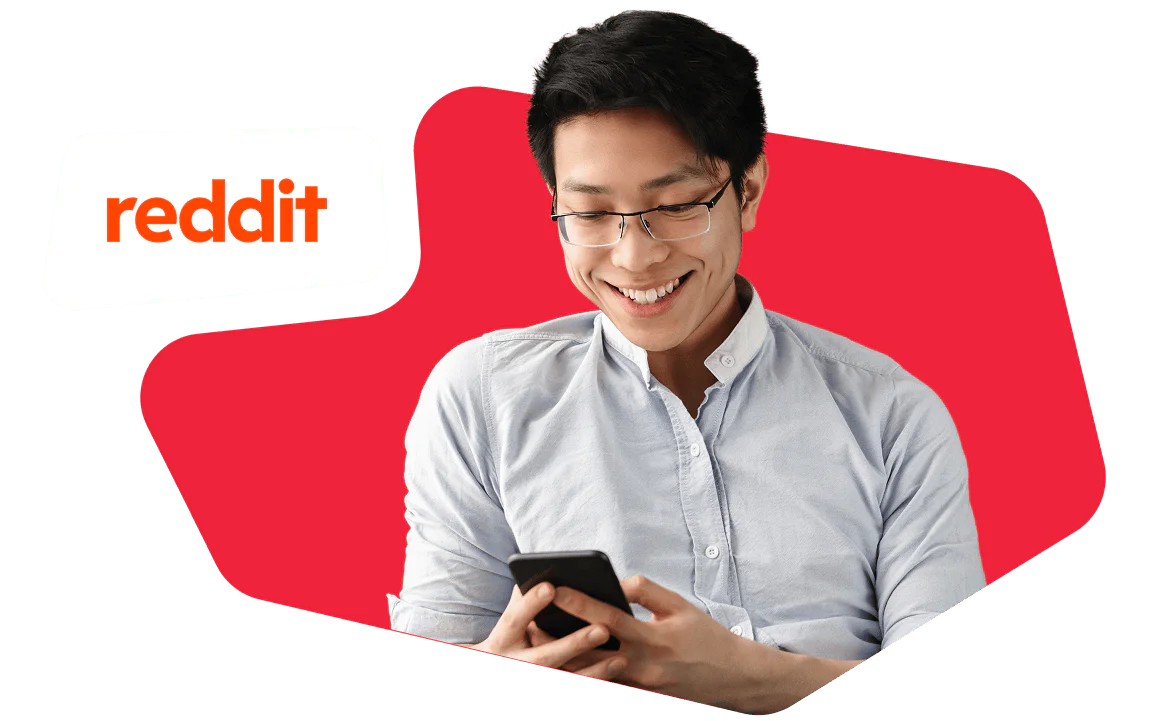 Man Smiling While Using Smartphone A man with glasses smiles while looking at a smartphone, with a Reddit logo in the background.