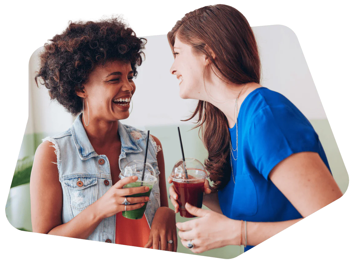 Two women enjoying conversation and drinks Two women smiling and holding drinks while talking inside a cafe.