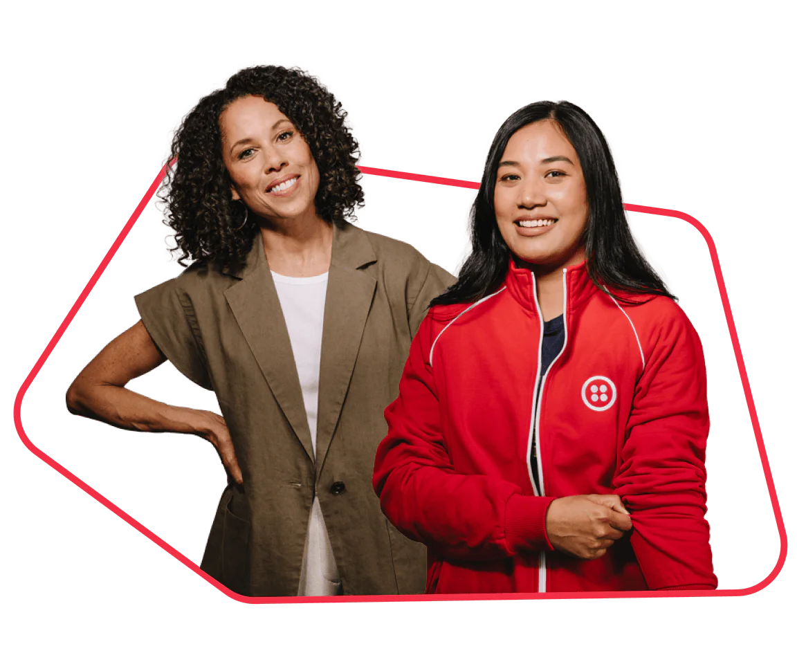 Two smiling women, one in a casual blazer and the other in a red athletic jacket, posing together.