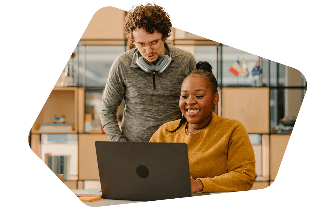 Smiling woman working on a laptop with a man standing behind her, both in a modern office.