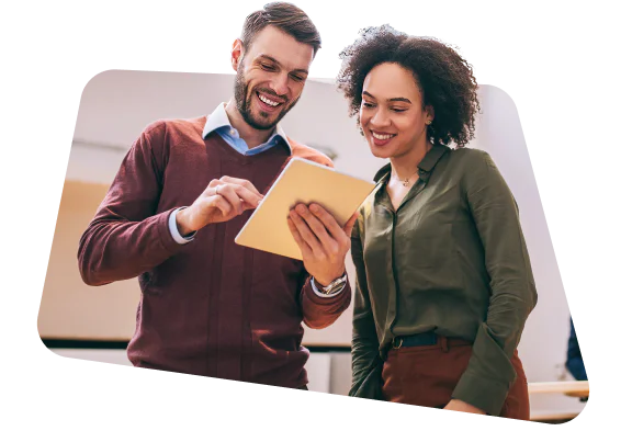 Two colleagues smiling while looking at a tablet together in an office setting.
