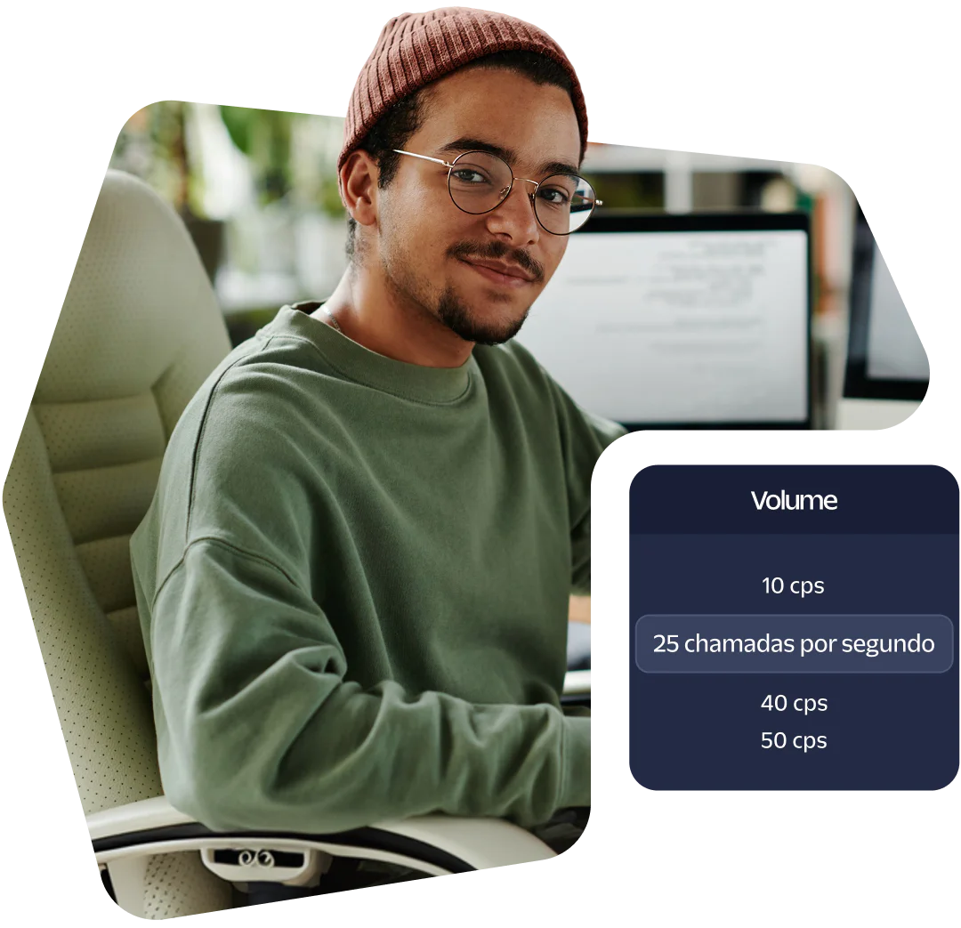 A person wearing glasses and a beanie sitting at a desk with a computer screen showing call volume data.